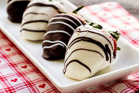 White chocolate and dark chocolate covered strawberries on white plate with heart patterned napkinの写真素材