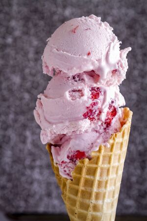 Double scoop of fresh strawberry ice cream in waffle cone against dark textured backgroundの写真素材