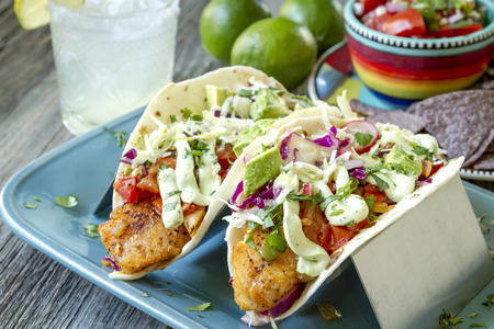 Plate of fish tacos with salsa, avocado, coleslaw and lime creme sitting on blue plateの写真素材