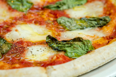 Close up of organic basil and mozzerella margherita pizza sitting on white plate on wooden table