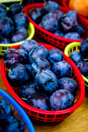 Colorful baskets filled with blue plums for sale at local farmers marketの写真素材