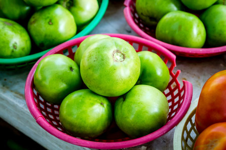 Green tomatoes in colorful plastic baskets for sale at local farmers marketの写真素材