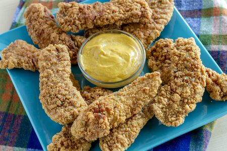 Honey mustard dipping sauce surrounded with fried chicken tenders sitting on blue square plateの写真素材