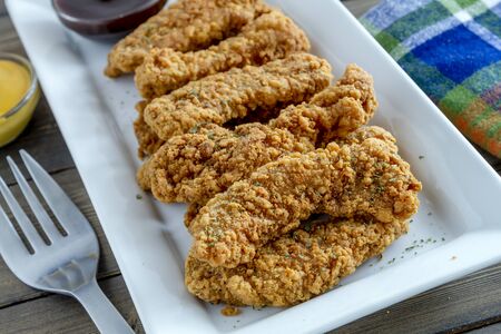 Fried chicken fingers on white platter with barbeque and honey mustard dipping sauceの写真素材
