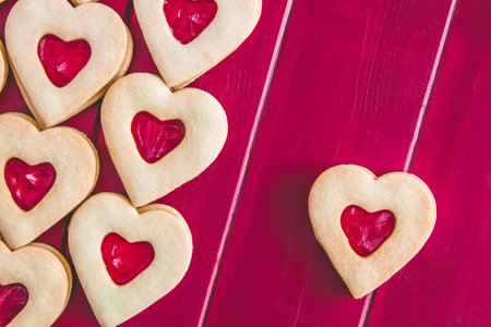 Heart shaped strawberry jam filled cookies on red wooden background with blank space