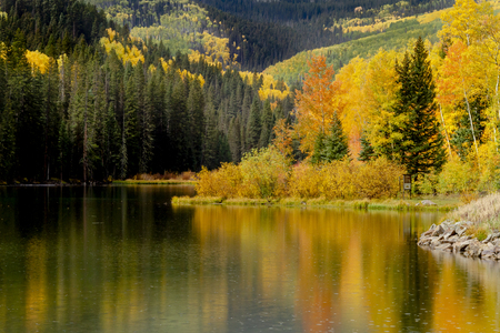 Fall afternoon sunshower reflecting in mountain lake with changing aspen trees and pine forest on the shoreの写真素材