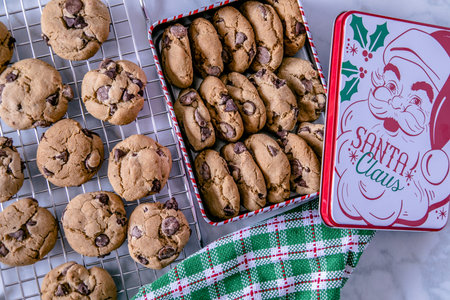 Close up of  chocolate chip cookies in retro Santa cookies tin and green plaid baking towel with...