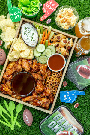 Overhead shot of football game day tailgate party food and snacks with wings, wieners, chips, dips and sauces with football themed decorationsの写真素材