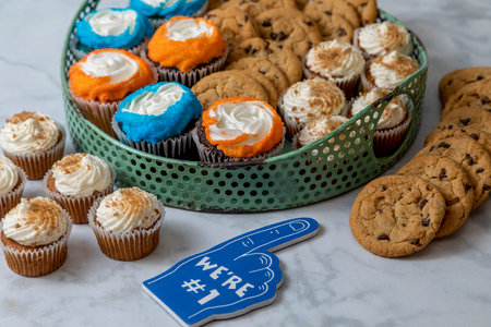 Display of desserts for football tailgating celebration with carrot cake cupcakes, chocolate chip cookies and vanilla and chocolate cupcakes with blue and orange sprinklesの写真素材