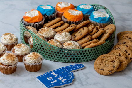 Football party dessert sweet display with bite sized carrot cake cupcakes, chocolate chip cookies and vanilla and chocolate cupcakes with orange and blue sprinklesの写真素材