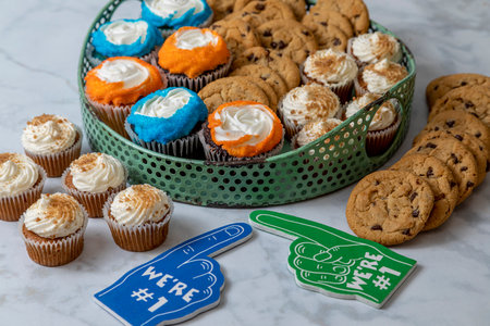 Football tailgating party dessert sweets display with bite sized carrot cake cupcakes, chocolate chip cookies and vanilla and chocolate cupcakes with orange and blue sprinkles and decorationsの写真素材