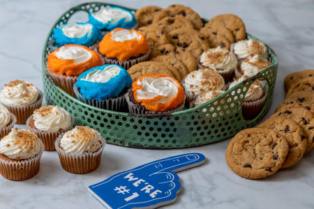 Football tailgating party dessert sweet display with bite sized carrot cake cupcakes, chocolate chip cookies and vanilla and chocolate cupcakes with orange and blue sprinklesの写真素材