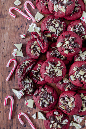 Close up of peppermint bark stuff red velvet cookies stacked on wooden table surrounded by peppermint bark candy pieces and small candy canes, shot from aboveの写真素材