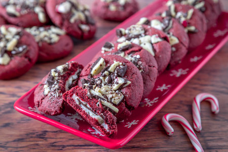 Close up of cookie display of peppermint bark stuffed red velvet cookies on a red plate with snowflakes, and stack of extra cookies in the background, candy canes in frontの写真素材