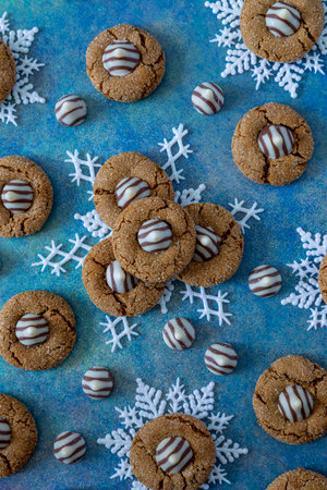 Close up of gingerbread blossom cookies, stacked on white glitter snowflakes sitting on blue abstract background, surrounded by white chocolate striped candy piecesの写真素材