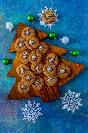Holiday cookie display of gingerbread blossom cookies sitting on wooden Christmas tree cutting board, on blue abstract background, with white snoflakes and Christmas ornamentsの写真素材