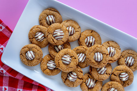 Gingerbread blossom holiday cookies, stacked on white rectangle plate with red and white heart checked napkin on pink backgroundの写真素材
