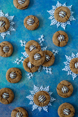 Gingerbread blossom holiday cookies, stacked on white glitter snowflakes sitting on blue abstract backgroundの写真素材