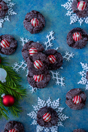 Close up of holiday cookie display of candy cane chocolate blossom cookies on white glitter snowflakes with pine tree branch, red and white ornaments, sitting on bright blue abstract backgroundの写真素材