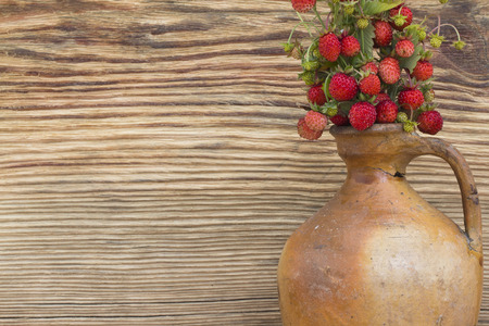 Forest berry - strawberries close up in the old clay jug on a background of woodの写真素材