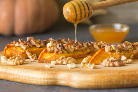 Authentic view of a pumpkin baked with slices of honey and walnuts on a wooden kitchen board....