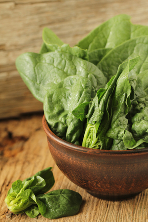 Fresh green leaves of spinach in a bowl on old wooden background. Top view.の写真素材