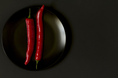Chili pepper on a plate on a black background. Black and red. Abstraction. Minimalism.Top view.