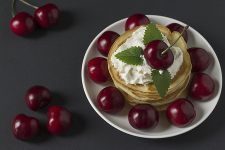 Pancakes with cherries and whipped cream on a black backgroundの写真素材
