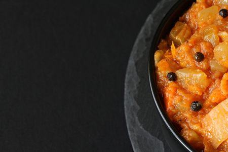 Vegetarian ragout of summer vegetables (zucchini, carrots, tomatoes, spices, garlic) in a bowl on a black backgroundの写真素材