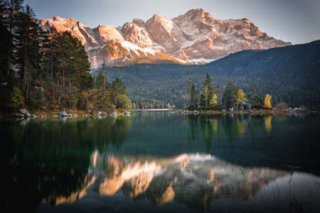 Photo Eibsee in the municipality of Grainau with the Wetterstein Mountains, forest and the Zugspitze at sunset. The Eibsee is a popular destination in Bavaria below the Zugspitze.の写真素材