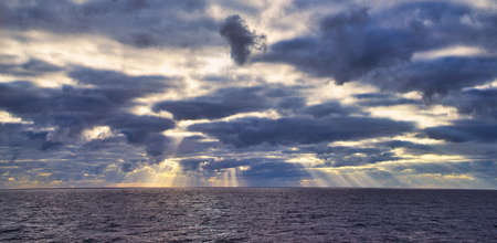 Sun rays passing through dark clouds. The unpredictable drama of the sky. A view from a tourist cruise ship sailing in the North Pacific Ocean. June 2019の写真素材