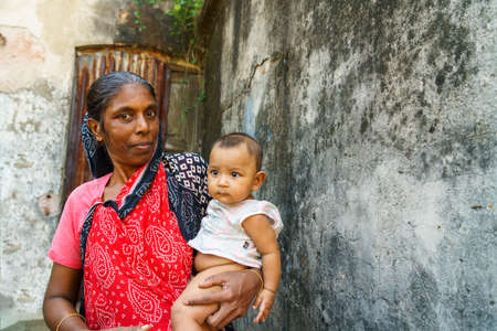 Dhaka, Bangladesh-November 14, 2019: Unidentified Bangladeshi woman holding small baby in her hands. The woman is smiling and she has ornaments on her nose. The location is a street corner in Dhaka city.のeditorial素材