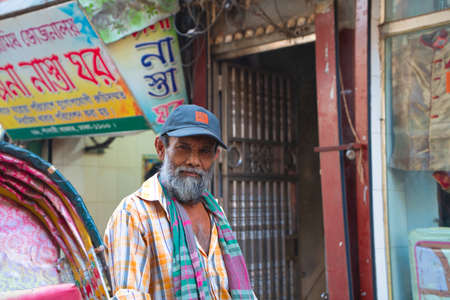Dhaka, Bangladesh-November 14, 2019: A brightly colored rickshaw. he main means of transportation on the local streets. Unidentified rickshaw driver. He wears a blue hat and has many white beards. Looking at the camera with a calm expression.のeditorial素材