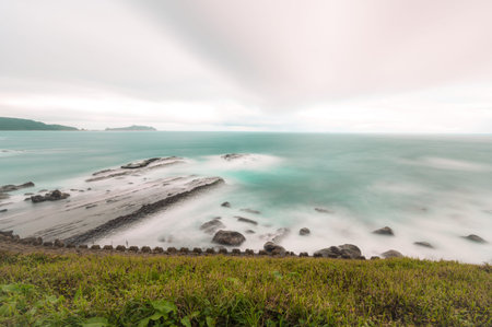 Rocky coast under blue sky and white clouds. White waves and light blue sea. Waimushan Seaside...