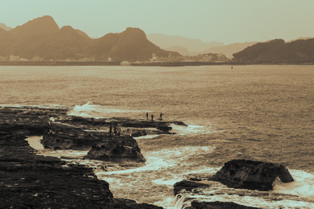 White waves lap against the rocks. Some people stood on the rocks and fished. Ruifang Rocky Beach, New Taipei City, Taiwan.の写真素材