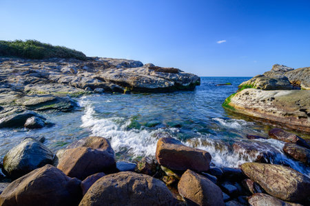 Calm and clear waters flow into small coves. Some green algae grow on rocks. The peculiar rocky...