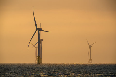 Fans of wind turbines spin over the sparkling sea. An offshore wind farm off the northwest coast of...