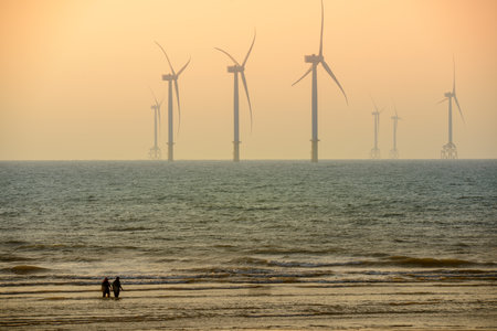 Fans of wind turbines spin over the sparkling sea. Dynamic clouds at sunset. An offshore wind farm off the northwest coast of Taiwan. One of green power.の写真素材