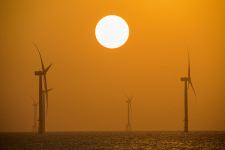 Fans of wind turbines spin over the sparkling sea. Dynamic clouds at sunset. An offshore wind farm...