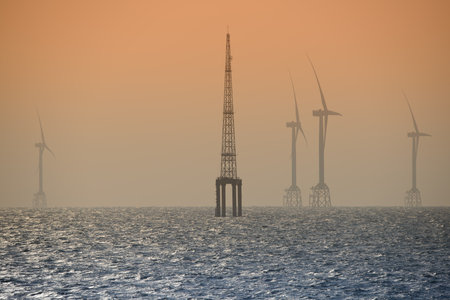 Fans of wind turbines spin over the sparkling sea. An offshore wind farm off the northwest coast of Taiwan. One of green power.の写真素材