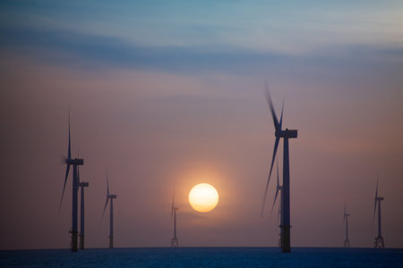 Fans of wind turbines spin over the sparkling sea. Dynamic clouds at sunset. An offshore wind farm off the northwest coast of Taiwan. One of green power.の写真素材