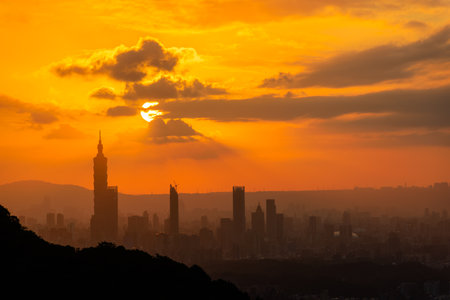 At dusk, the sun breaks through the clouds and shines on Taipei City. Silhouettes of city buildings. Orange sky and dark clouds.の写真素材