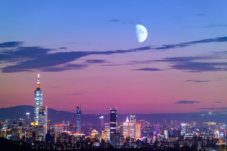 At night, the colorful lights gradually light up. The moon is also in the sky. Orange-red night view of the city after sunset in autumn. Taipei, Taiwan.の写真素材
