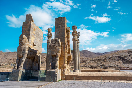 Imposing Lamassu statues stand tall, casting intricate shadows amidst the ancient ruins of Persepolis, Iran. Captured on a bright day with the blue sky and clouds.の写真素材