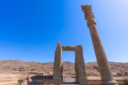 Imposing Lamassu statues stand tall, casting intricate shadows amidst the ancient ruins of Persepolis, Iran. Captured on a bright day with the blue sky and clouds.の写真素材
