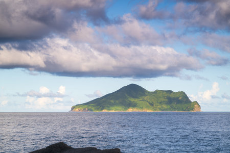 Distant view of Turtle Island standing in the sea, covered in lush green plants. White clouds slowly...