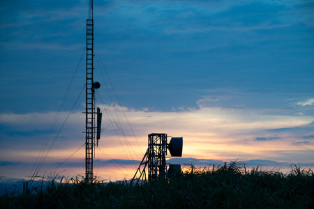 A striking sunset with vivid orange and purple hues over a radar station. Silhouetted communication...