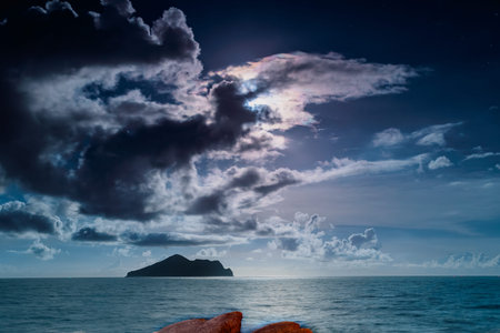 The full moon illuminates the tranquil night view of Turtle Island. The sky was filled with dramatic clouds in varying shades of purple and blue. Touzhen, Yilan County, Taiwan.の写真素材