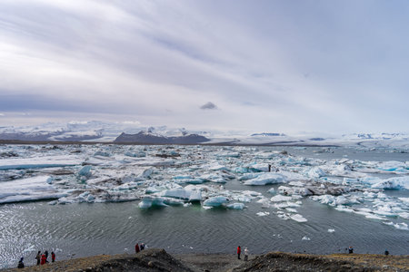 Blue and white icebergs float in a glacial lake against a backdrop of glaciers, creating a serene...