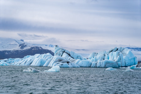 Blue and white icebergs float in a glacial lake against a backdrop of glaciers, creating a serene scene. Unspoiled Jokulsarlon, Iceland.の写真素材